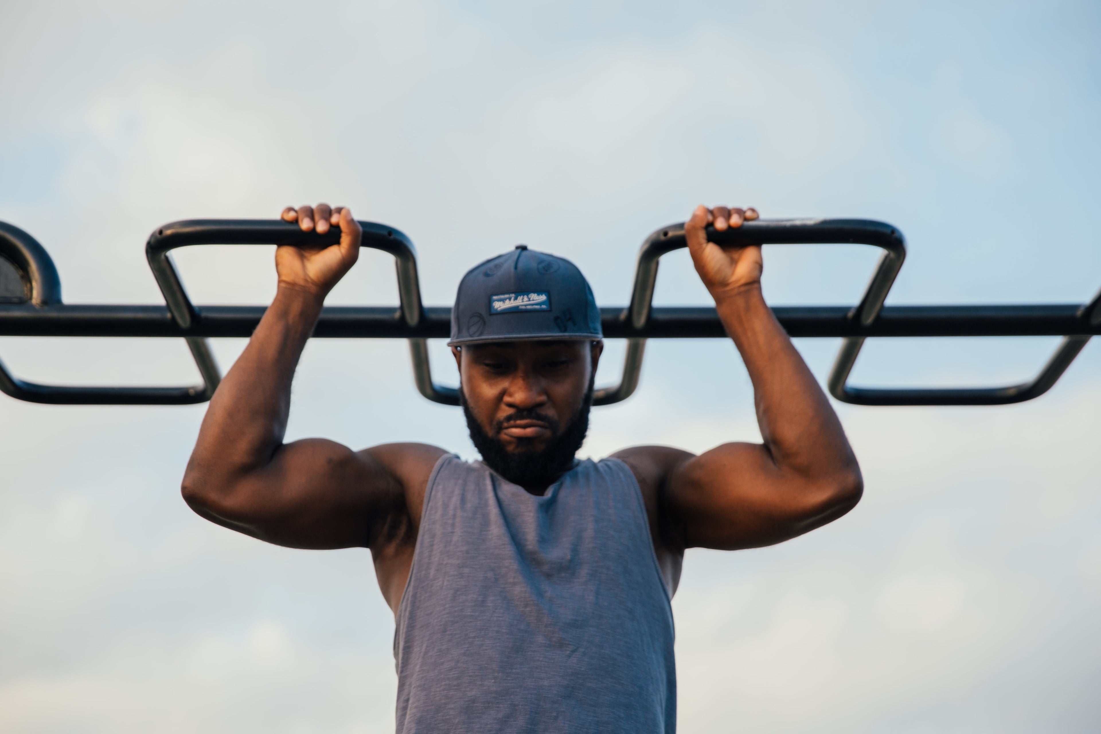 Man doing pull-ups on outdoor gym equipment with a clear sky background