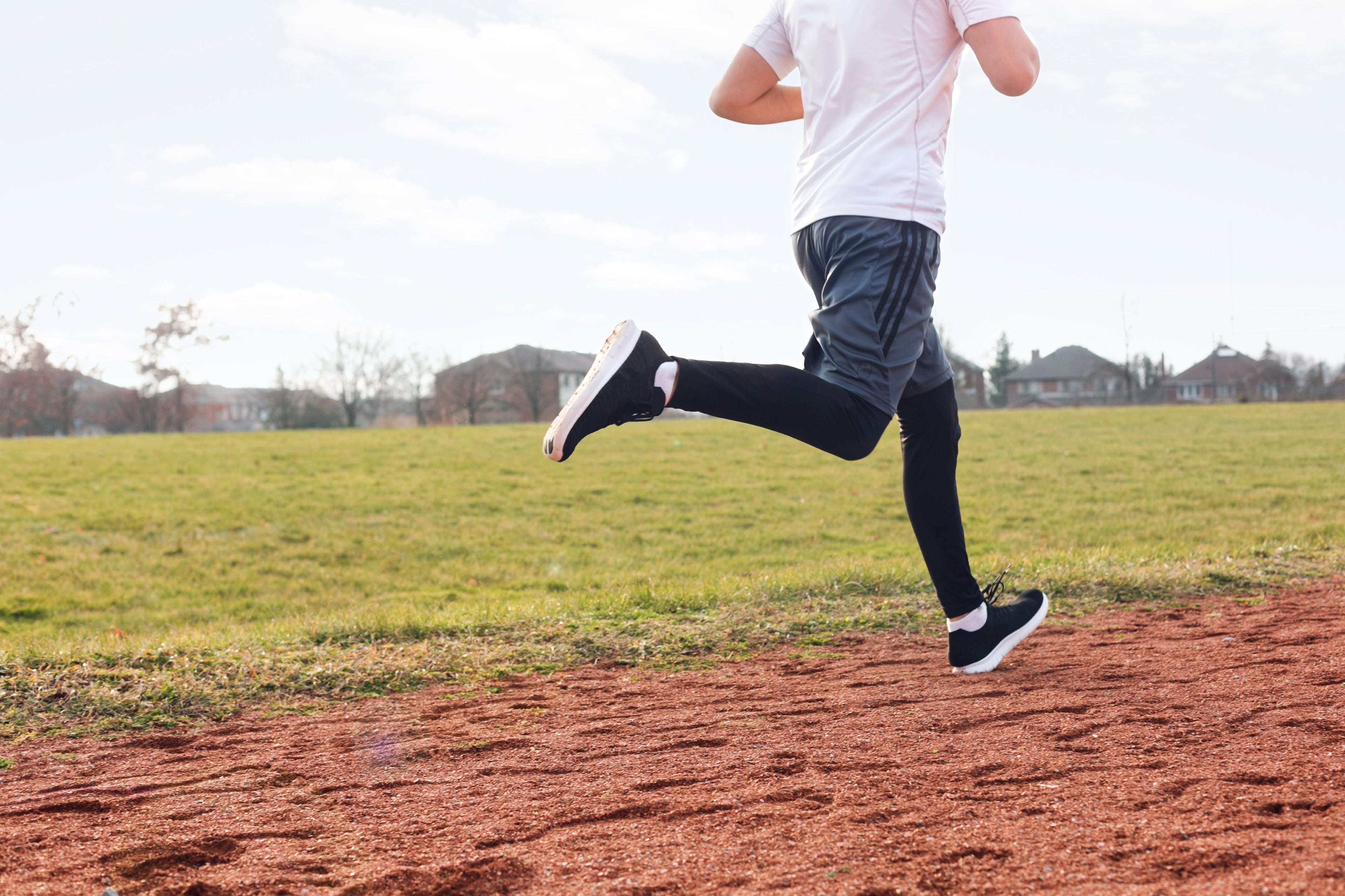 Person running on a dirt path with grass and houses in the background